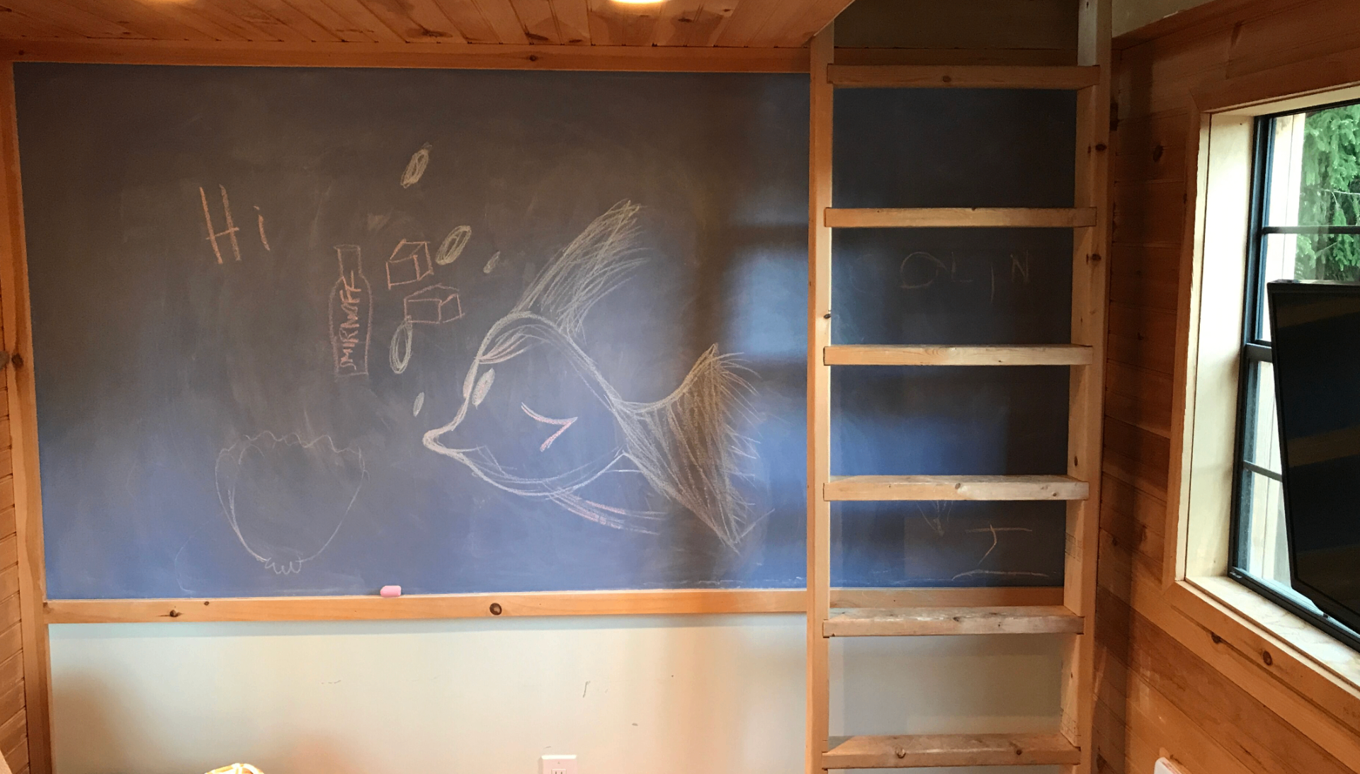 Treehouse chalkboard wall with chalk drawings and built-in ladder shelving