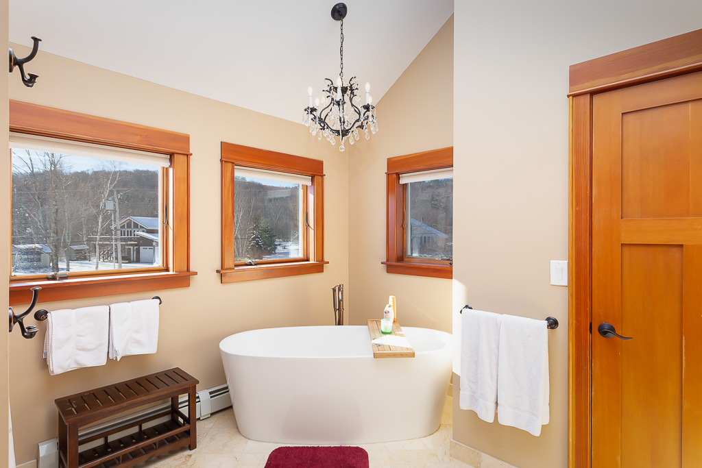 Primary bath with freestanding soaking tub, chandelier, and three mountain-view windows
