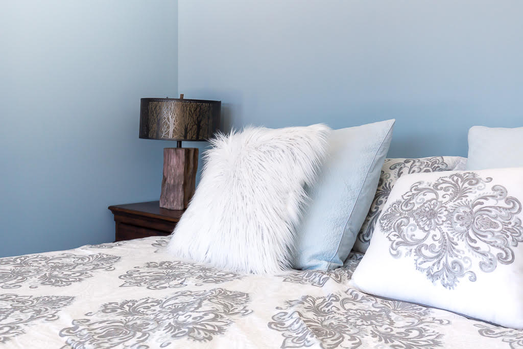 Blue guest bedroom detail with plush pillows and forest-lamp accent