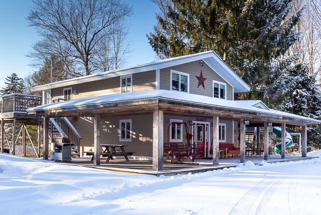 Snow-covered exterior of the Tree House Lodge with wraparound covered porch