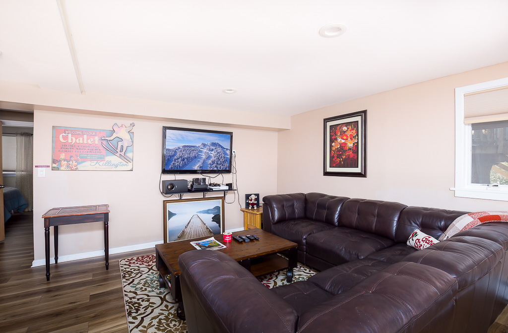 Lower-level rec room with sectional sofa, TV, and Killington chalet art