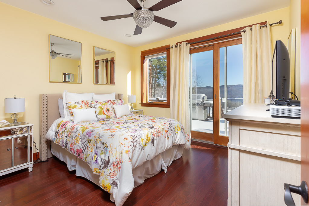 Yellow bedroom with floral bedding, mirrored nightstand, and sliding door to the deck