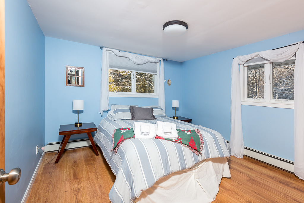 Sky-blue bedroom with striped linens, twin nightstands, and forest views
