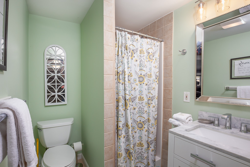Green-walled bathroom with marble vanity, tiled tub-shower, and paisley curtain
