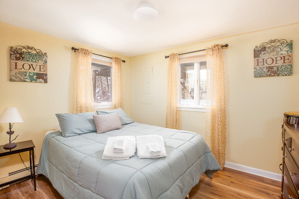 Sunny yellow bedroom with queen bed, 'Love' and 'Hope' wall art, and forest views