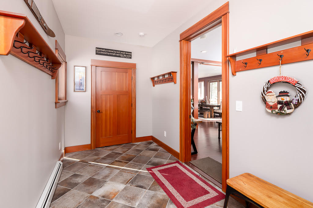 Mudroom hallway with wood coat racks, holiday wreath, and slate tile floor