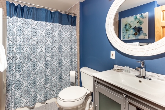 Navy bathroom with patterned shower curtain, oval mirror, and gray vanity