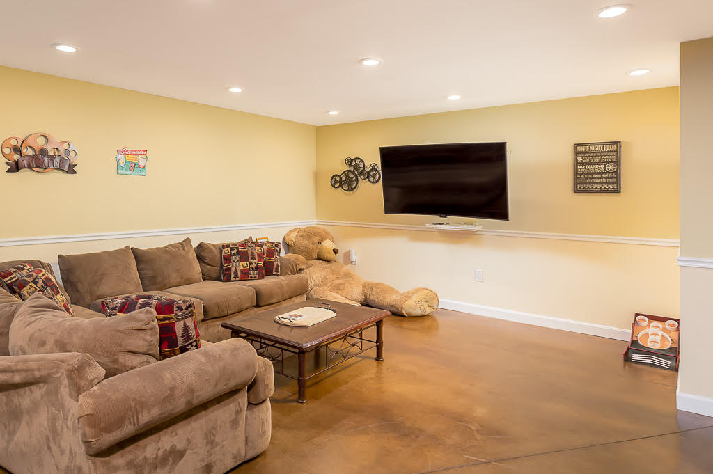 Lower-level media room with sectional sofa and giant teddy bear