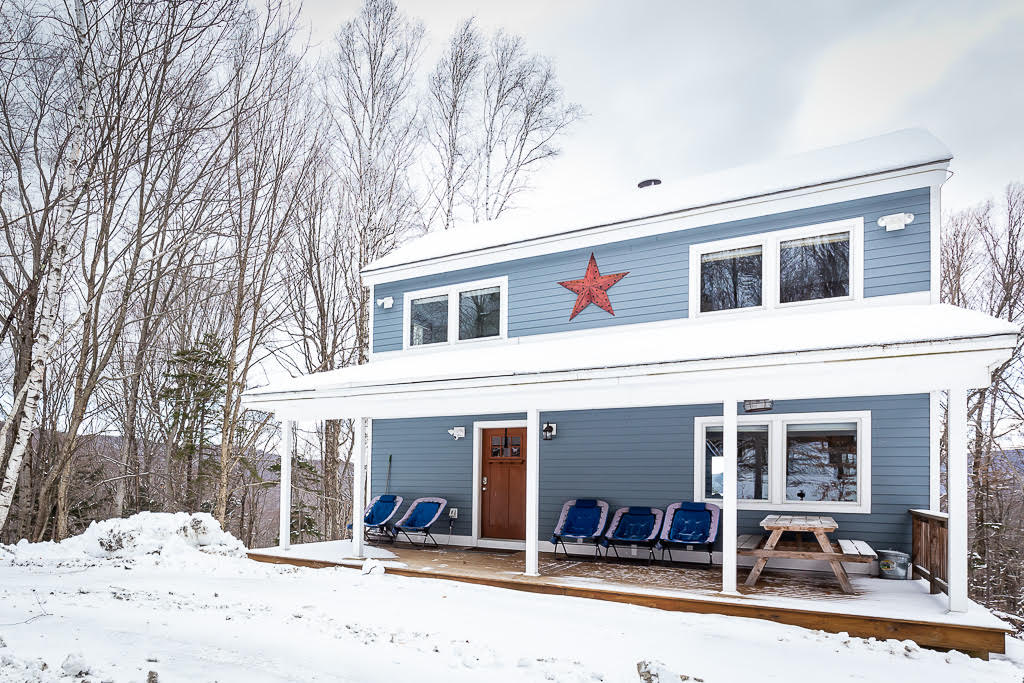 Blue cabin exterior with red star and covered porch in winter
