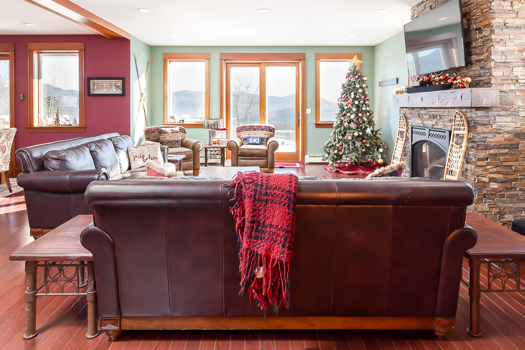 Great room at Christmas with leather sofas, stone fireplace, decorated tree, and mountain views
