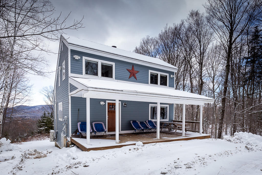 Side view of the blue ski house with mountain backdrop and snowy yard