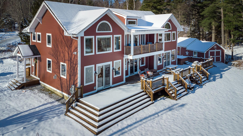 Aerial view of the red lodge in winter with wraparound deck and snow-covered yard