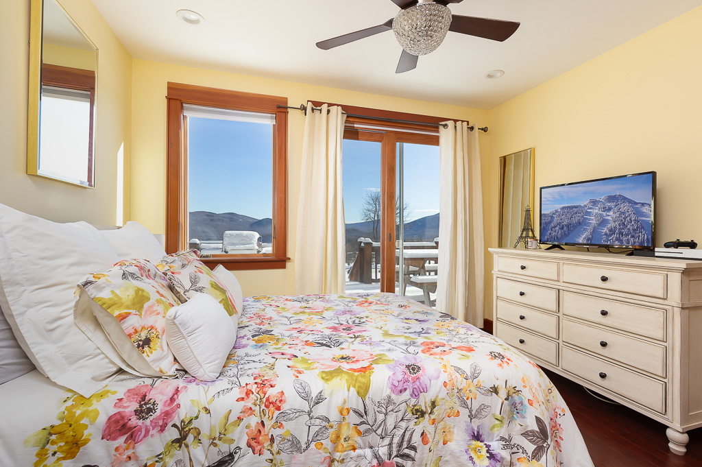 Yellow bedroom with floral bedding, dresser, and mountain views through the French doors