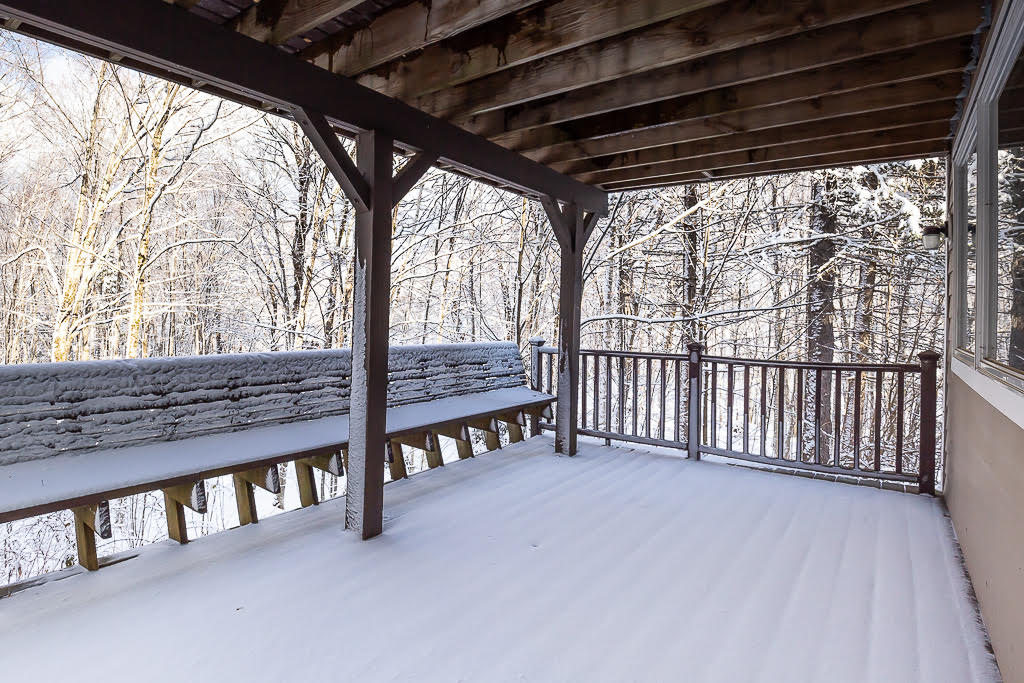 Covered wraparound deck overlooking snow-dusted Vermont woods