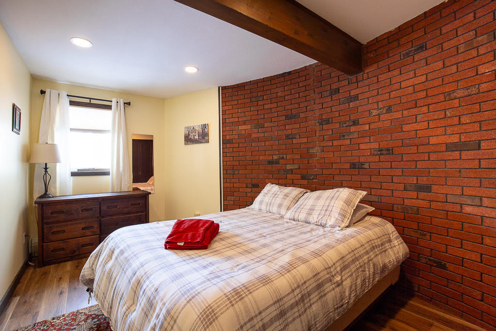 Queen bedroom with exposed brick accent wall and wood beam