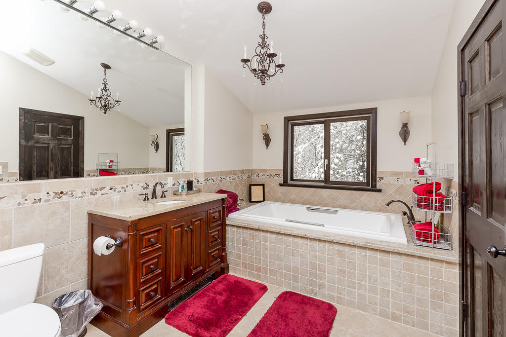 Primary bathroom with soaking tub, granite vanity, and forest views
