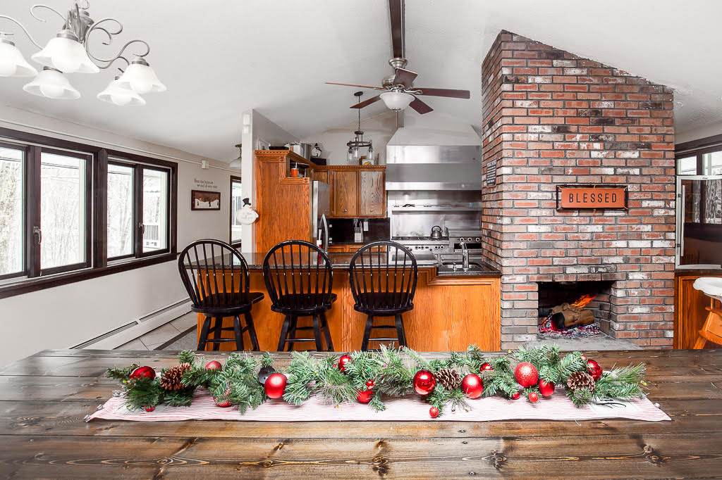 Open dining table beside the central brick fireplace and bar-seat kitchen