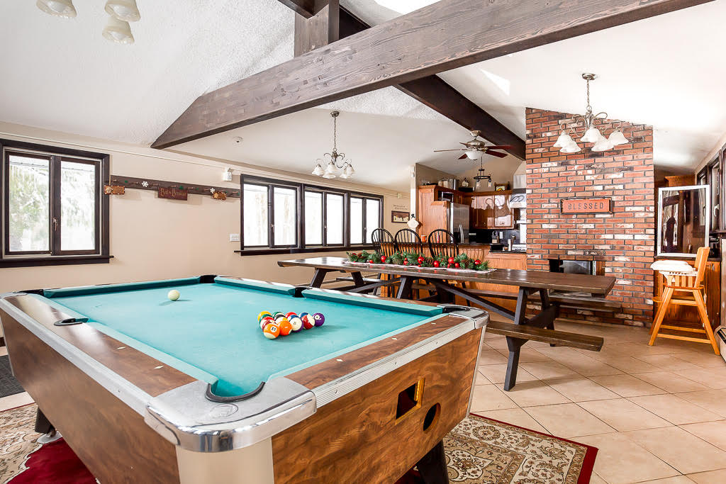 Pool table and long picnic dining table beneath exposed beams and brick