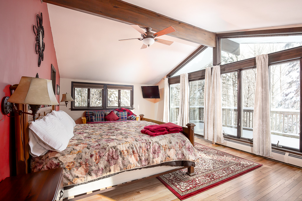 Primary bedroom with king bed, vaulted ceiling, and floor-to-ceiling windows onto snowy woods