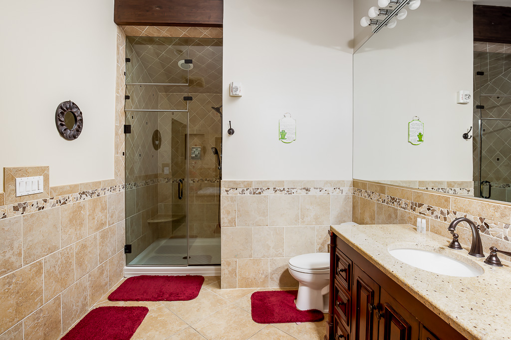 Spacious tiled bathroom with glass walk-in shower and granite double vanity