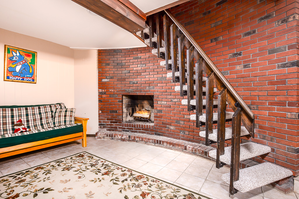 Lower-level lounge with brick fireplace, futon, and floating wood staircase